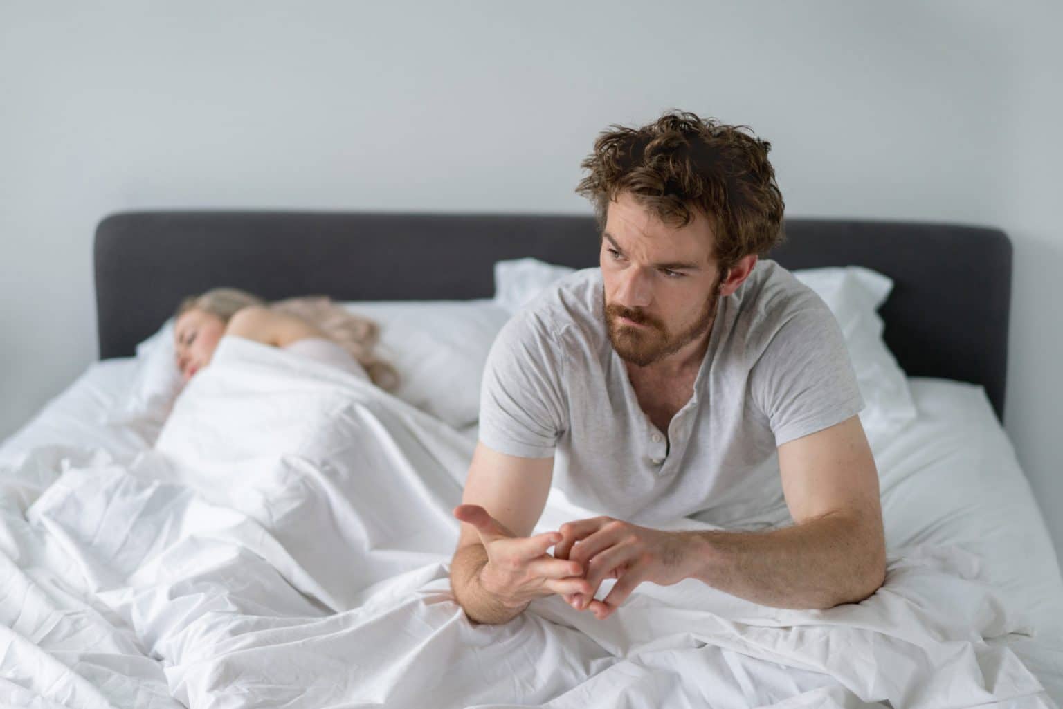 A man sitting up in bed thinking about his sleep issues.