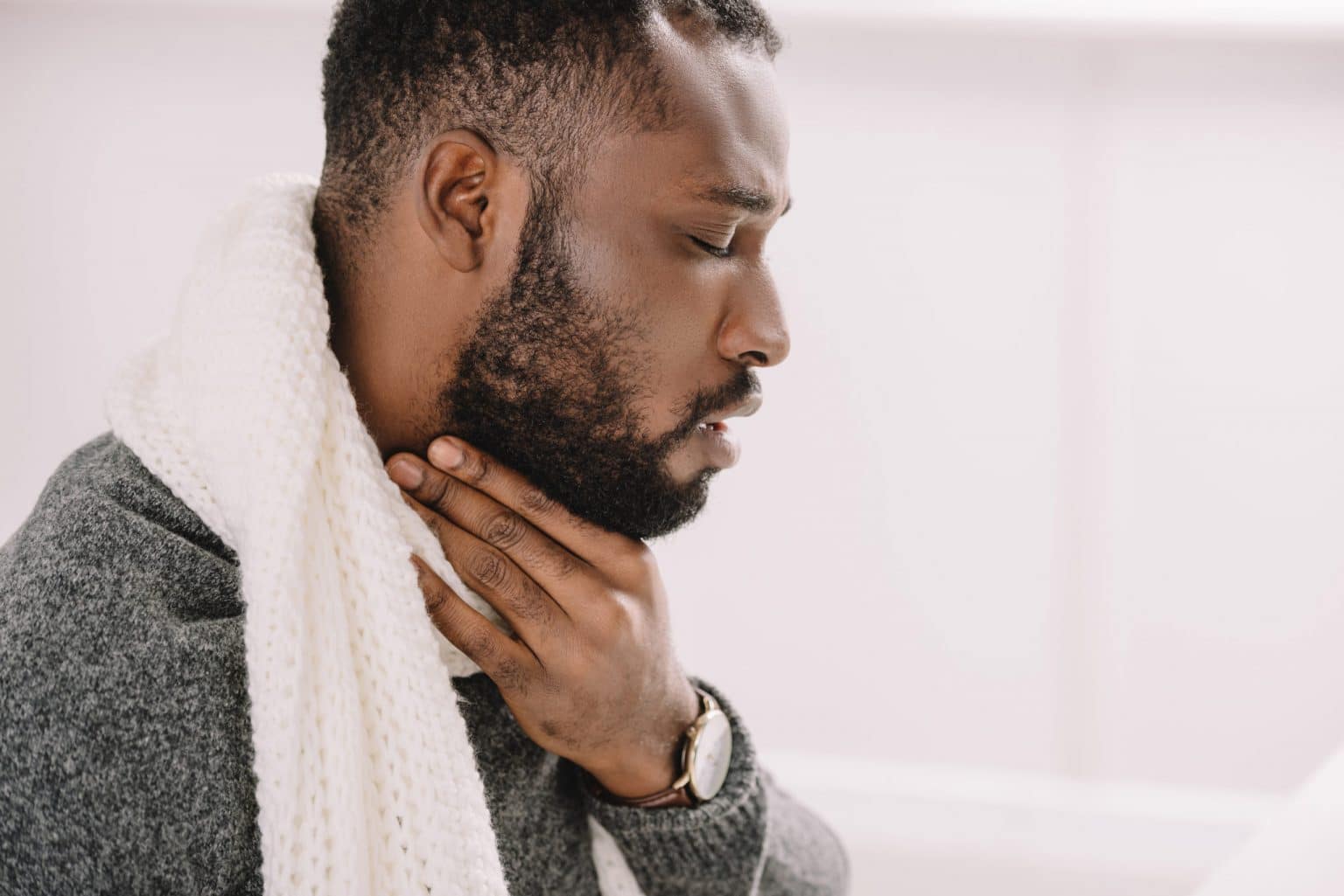 Side view of a man holding his throat with his mouth slightly open.